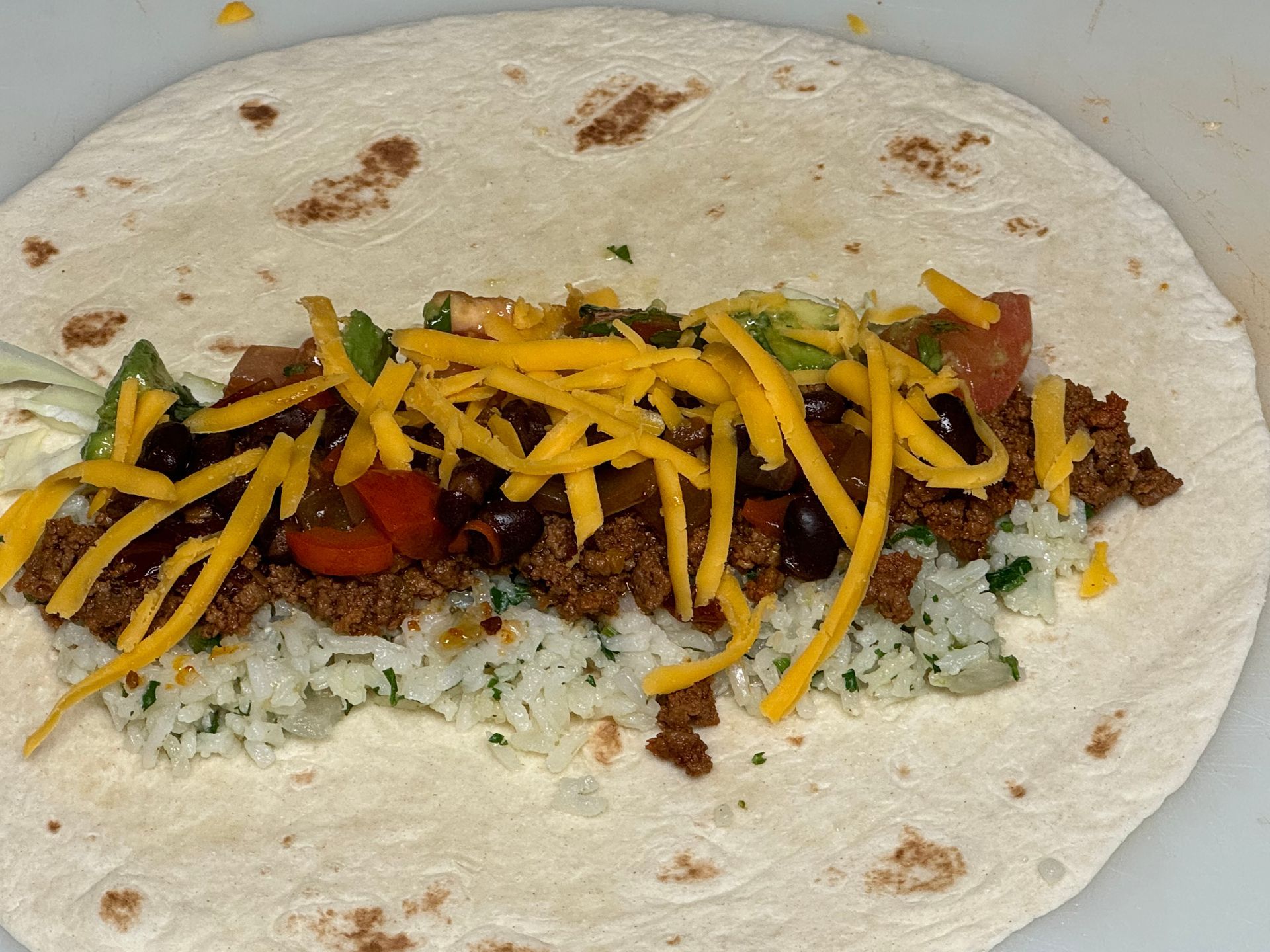 A tortilla with meat rice and cheese on it