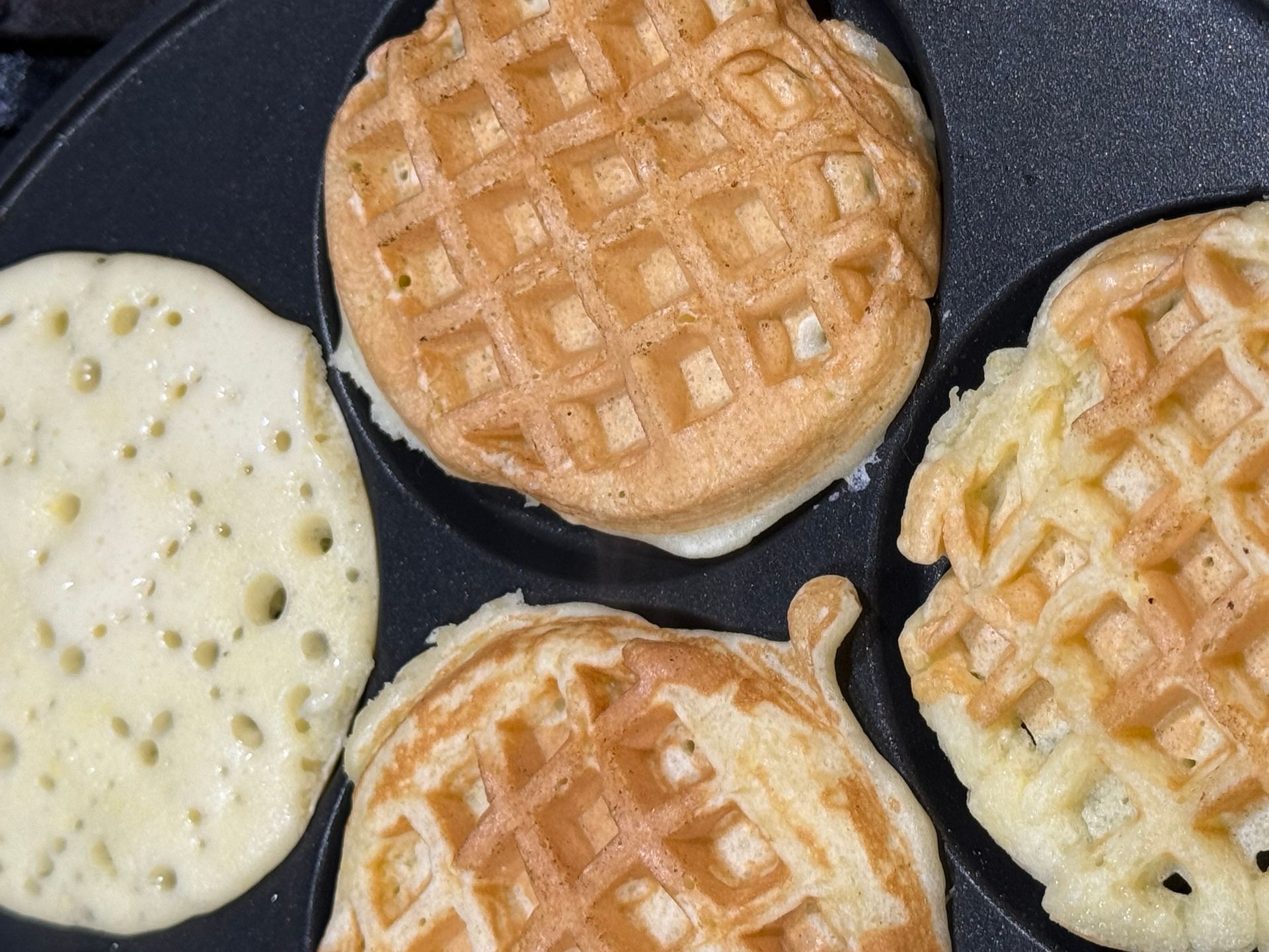 Four waffles are cooking in a pan on a stove top