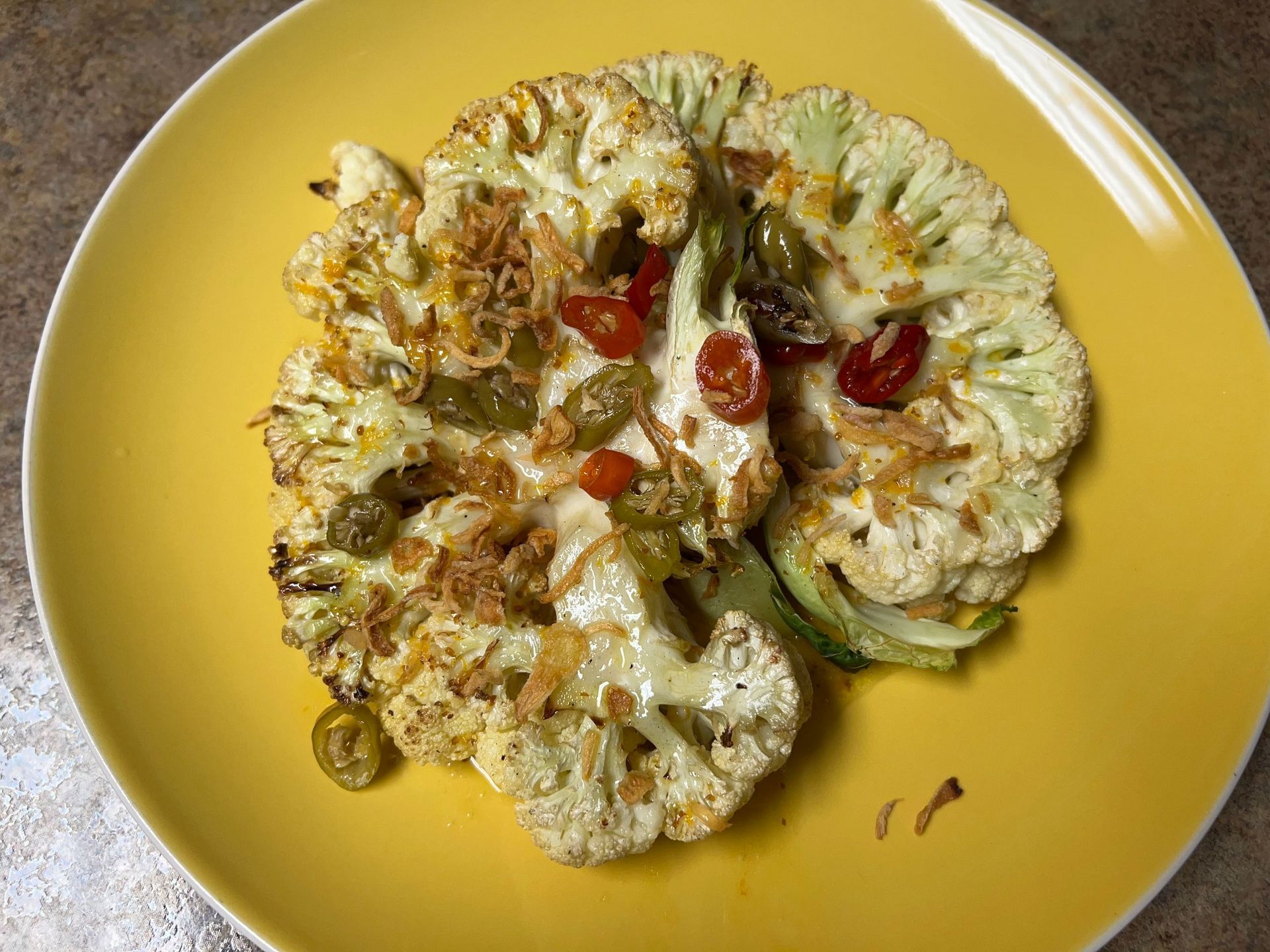 A yellow plate topped with roasted cauliflower and tomatoes