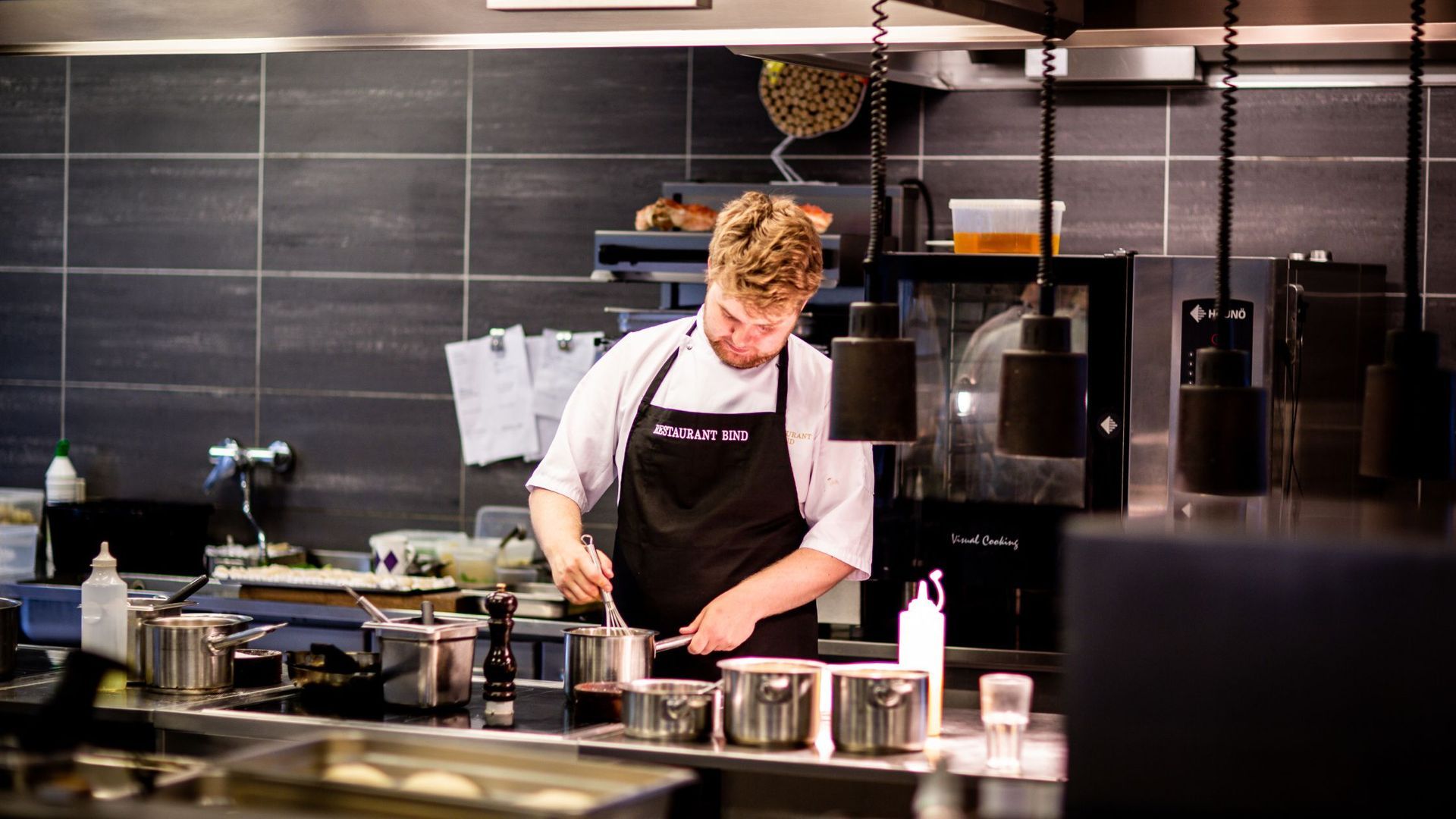 A man in an apron is preparing food in a kitchen.