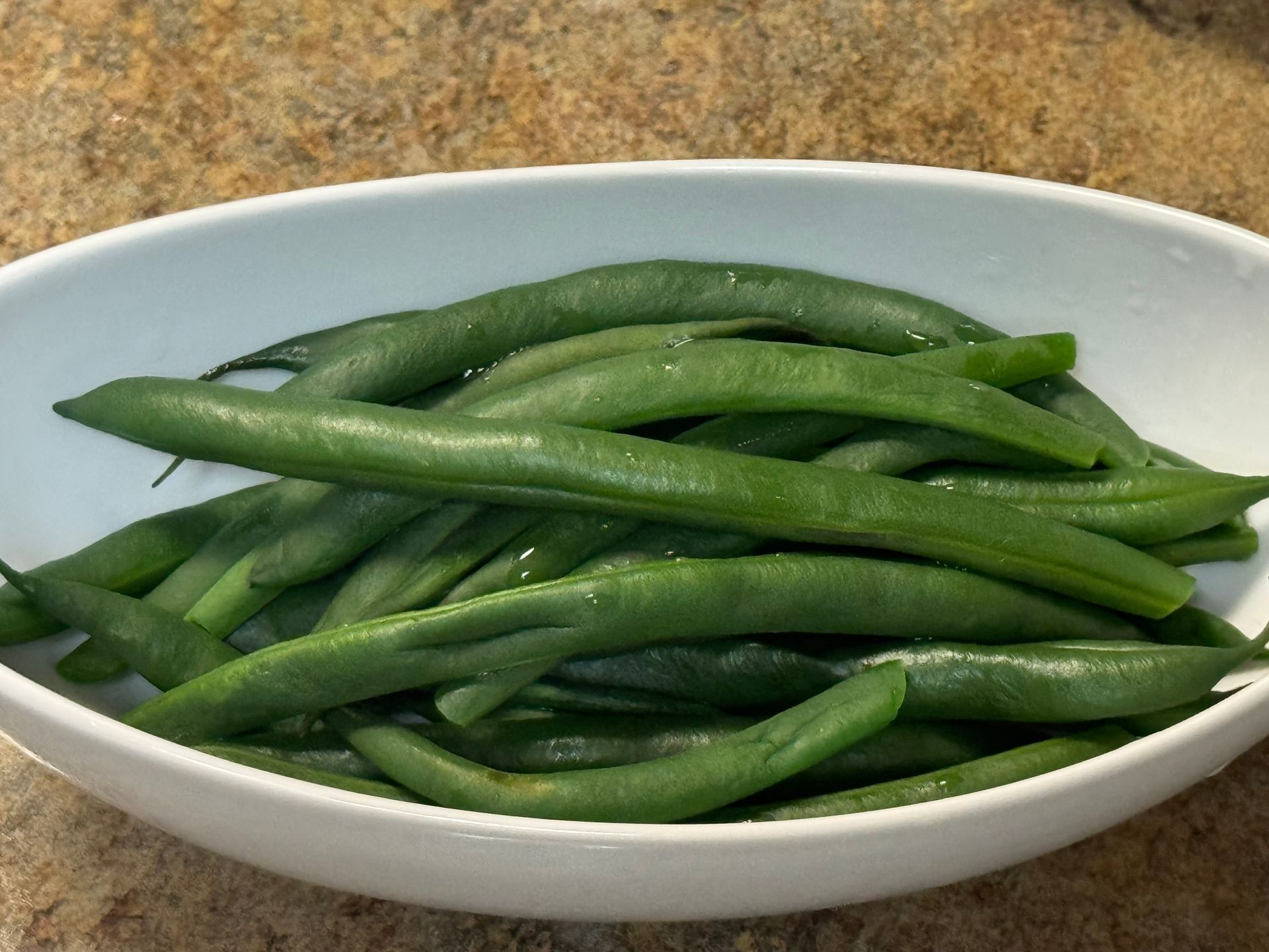 A white bowl filled with green beans on a table