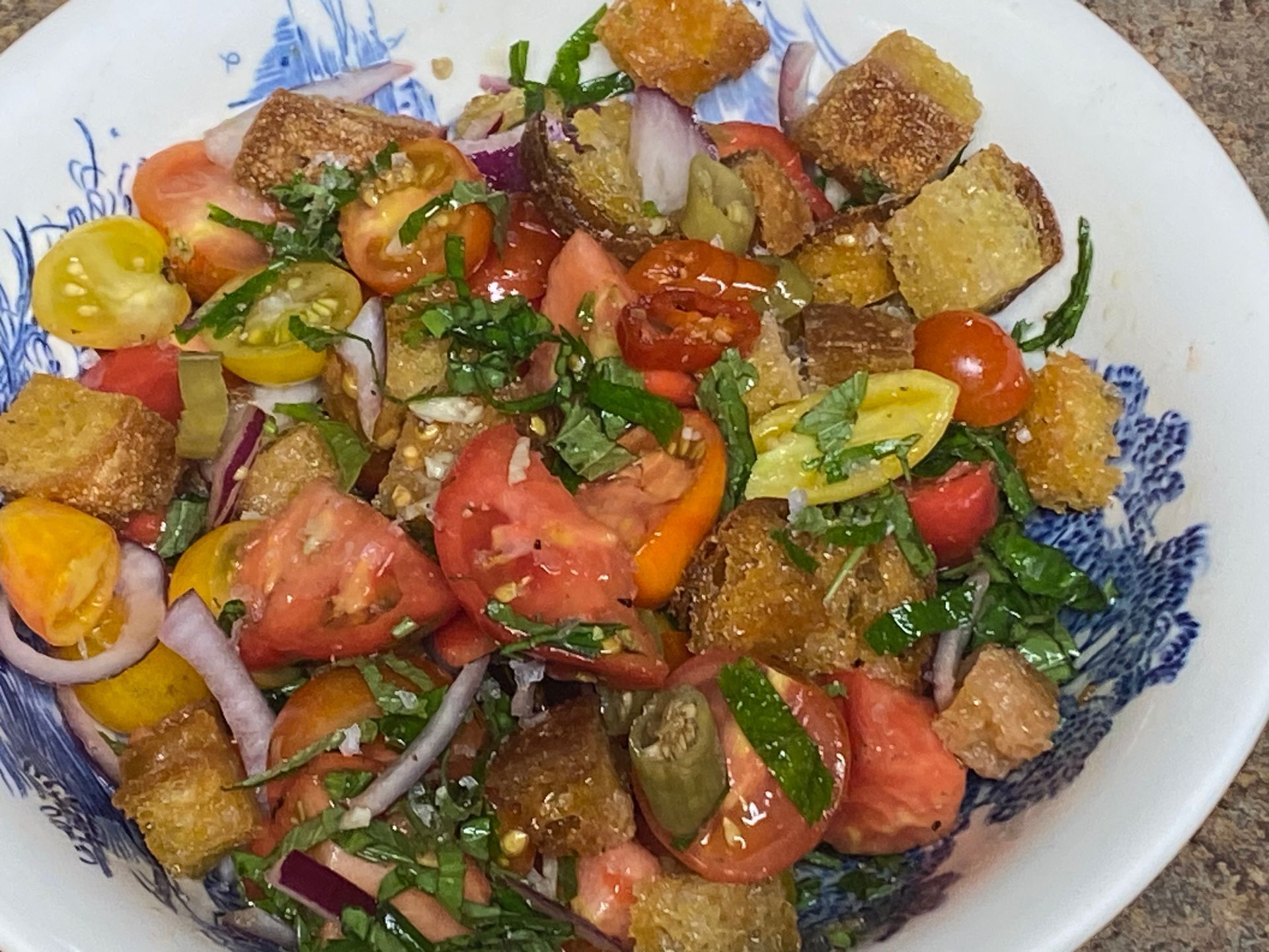 A salad with tomatoes , croutons , onions and other vegetables in a bowl