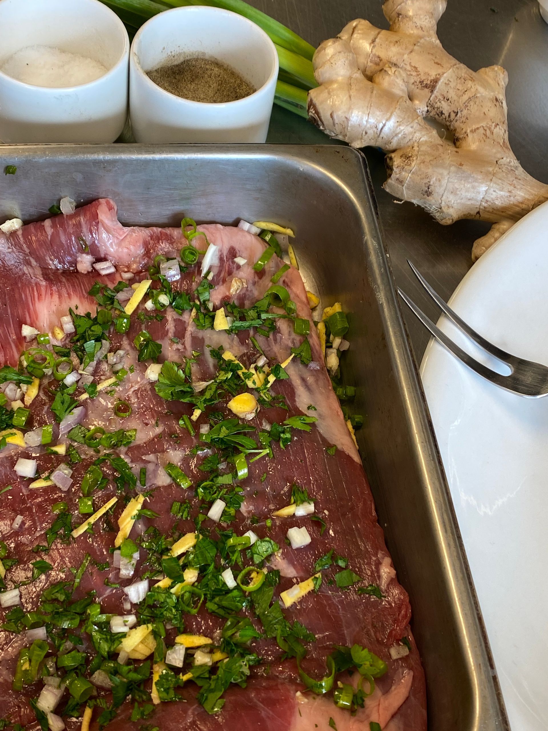 A pan filled with meat and vegetables next to a fork and ginger.