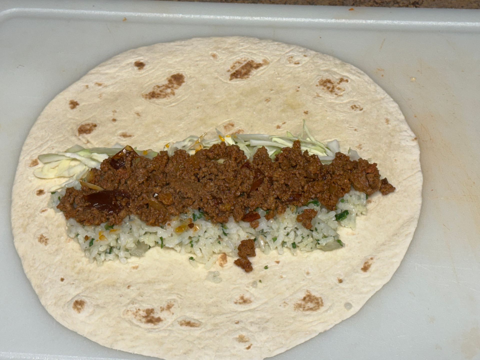 A close up of a tortilla with meat and rice on a cutting board.