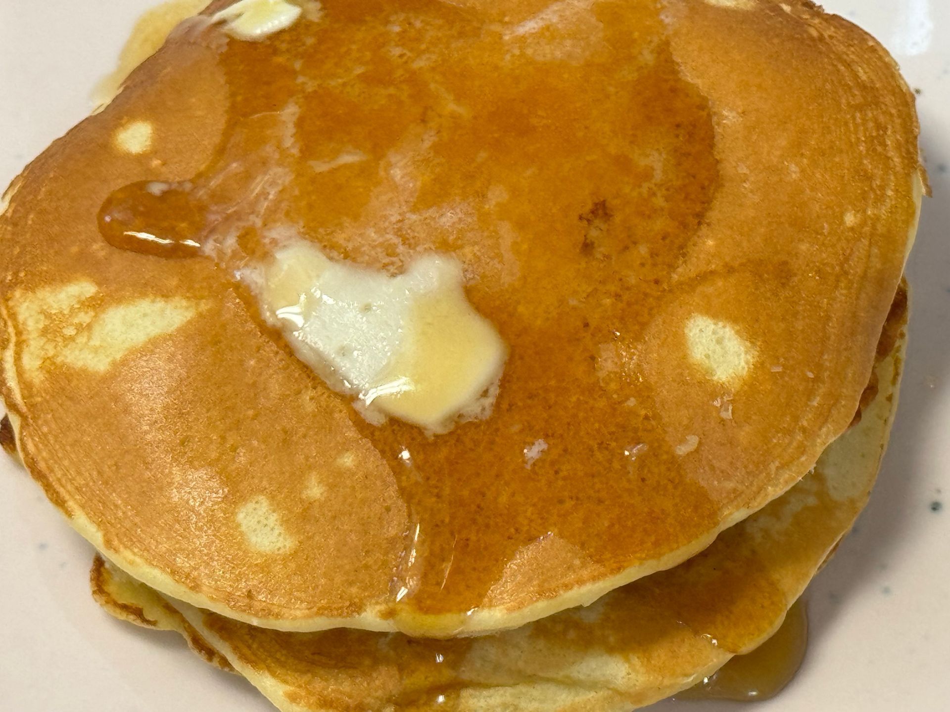 A stack of pancakes with syrup and butter on a white plate.