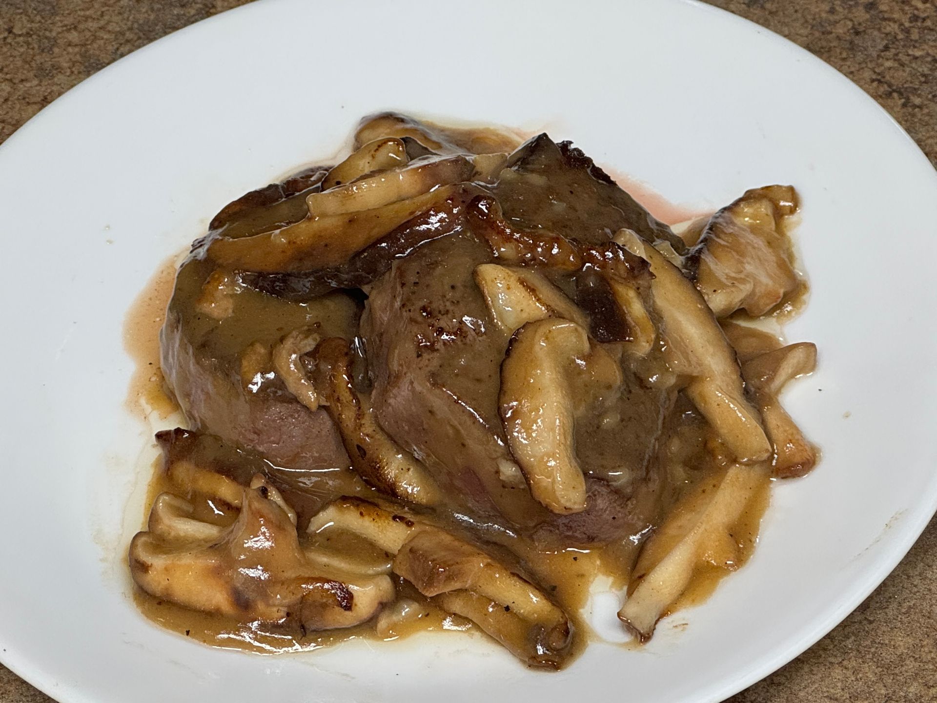 A steak with butter on top of it on a white plate