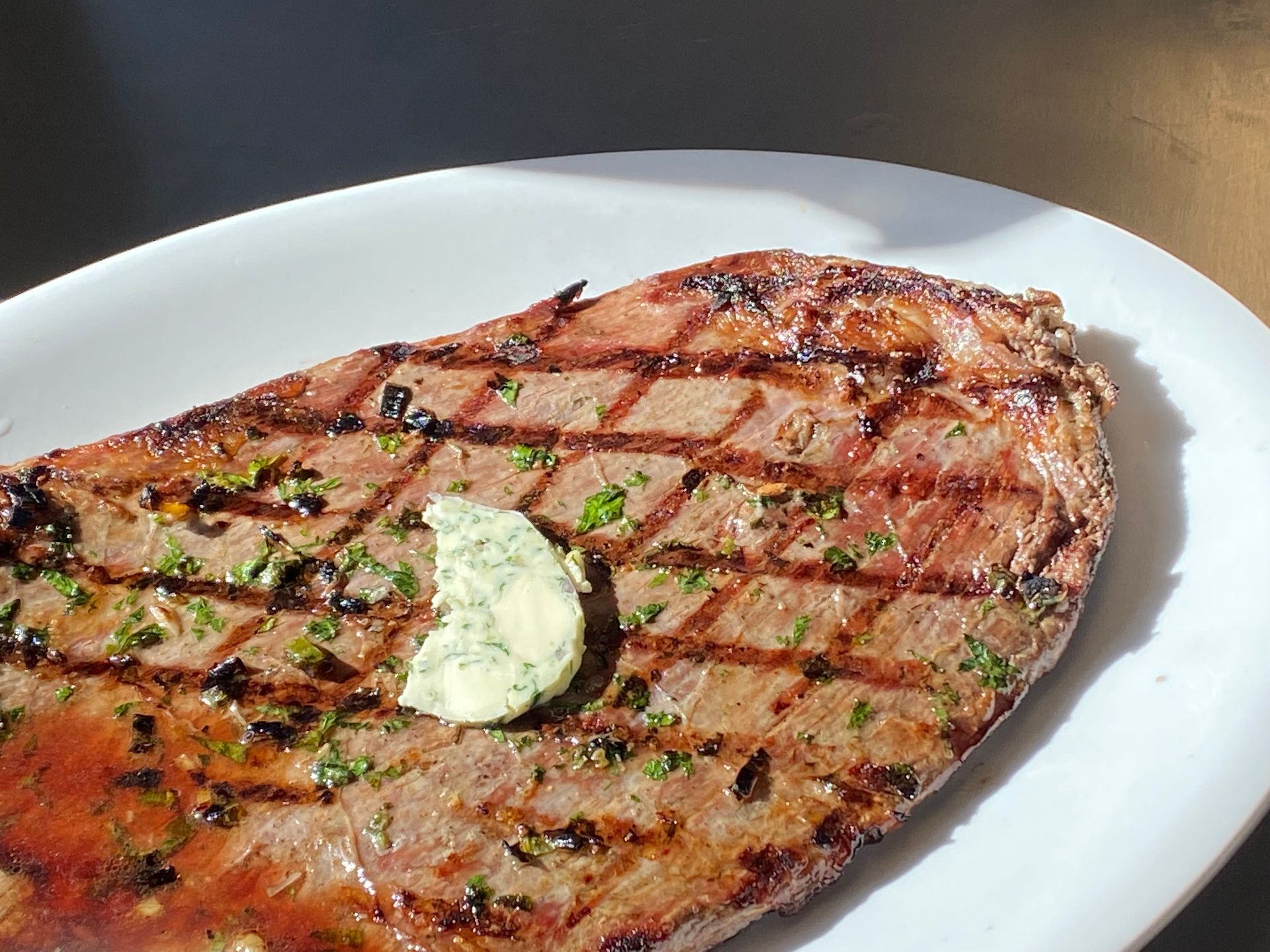A grilled steak on a white plate with butter on top