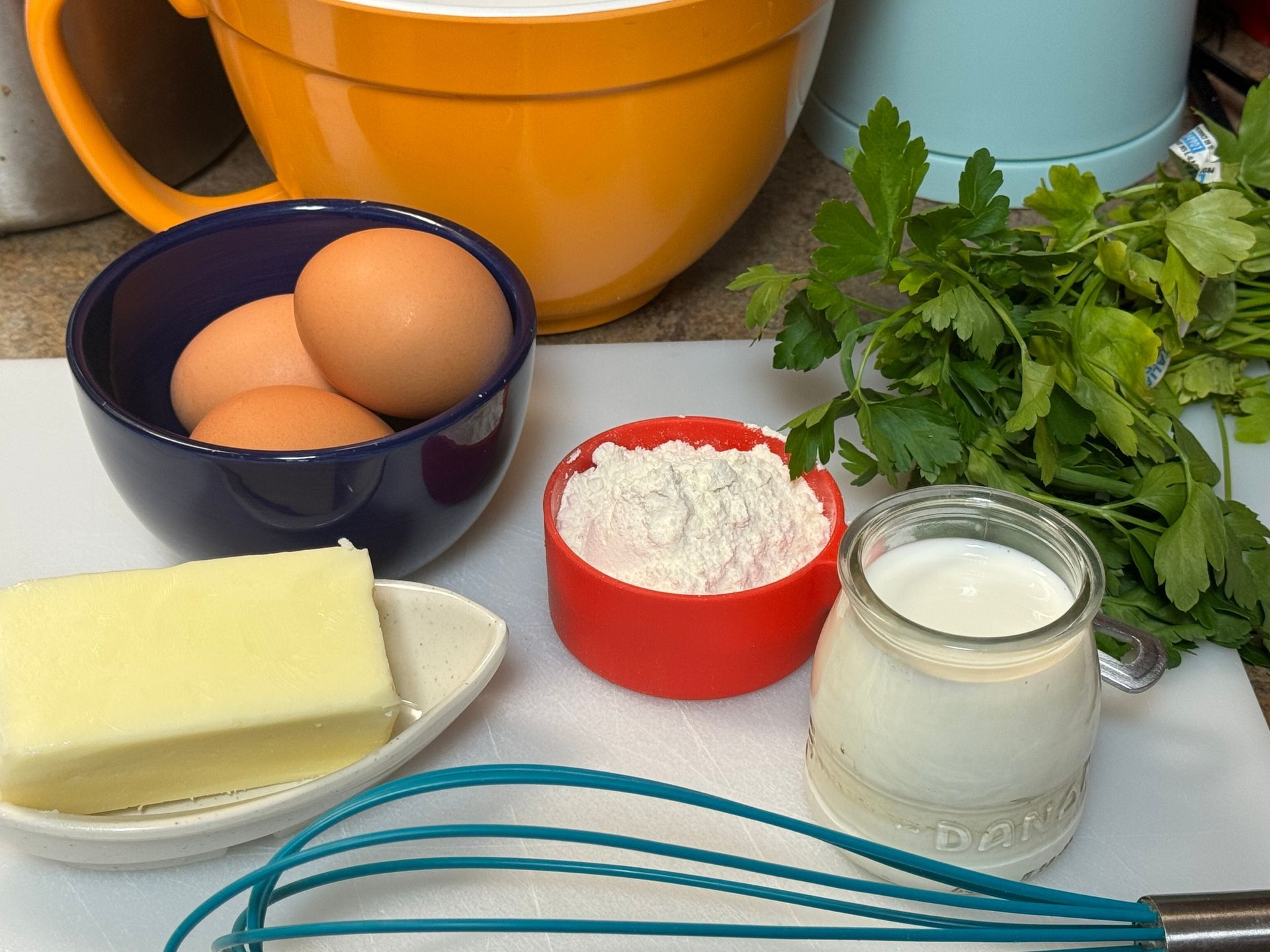 A cutting board with bowls of eggs butter flour and milk