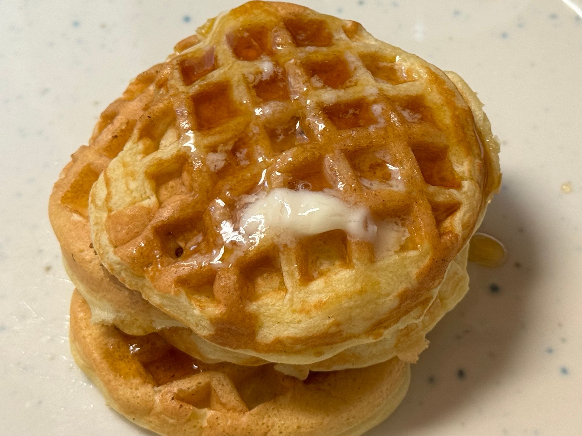 A stack of waffles with syrup and butter on a white plate.