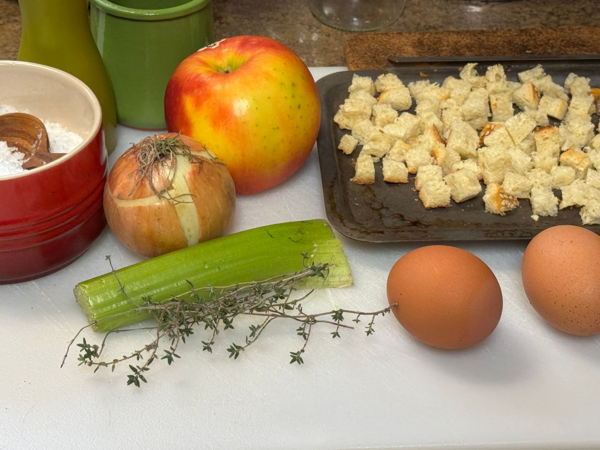 A cutting board with eggs , apples , celery , onions and croutons on it