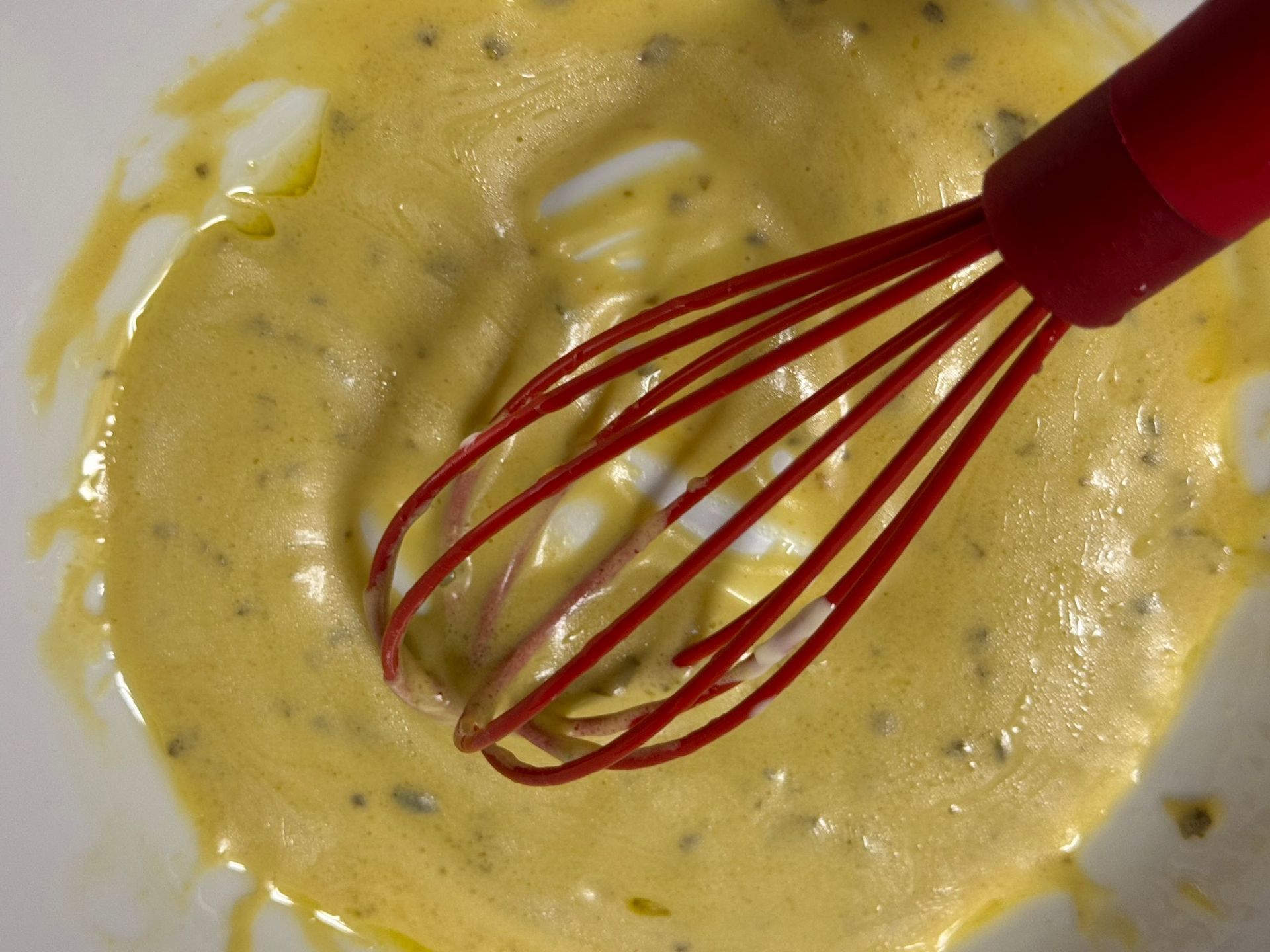A red whisk is in a bowl of sauce