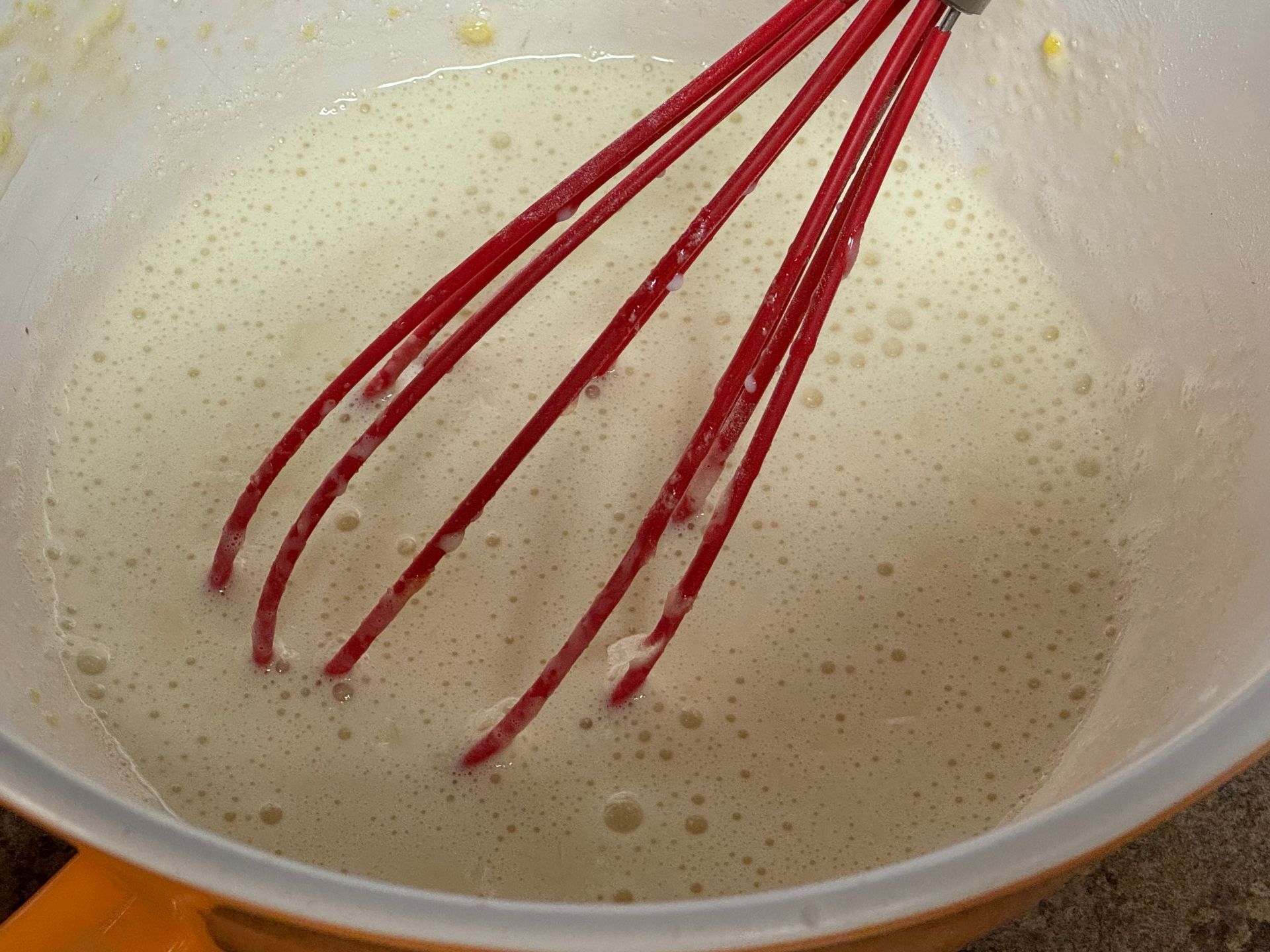 A red whisk is in a bowl of foamy liquid