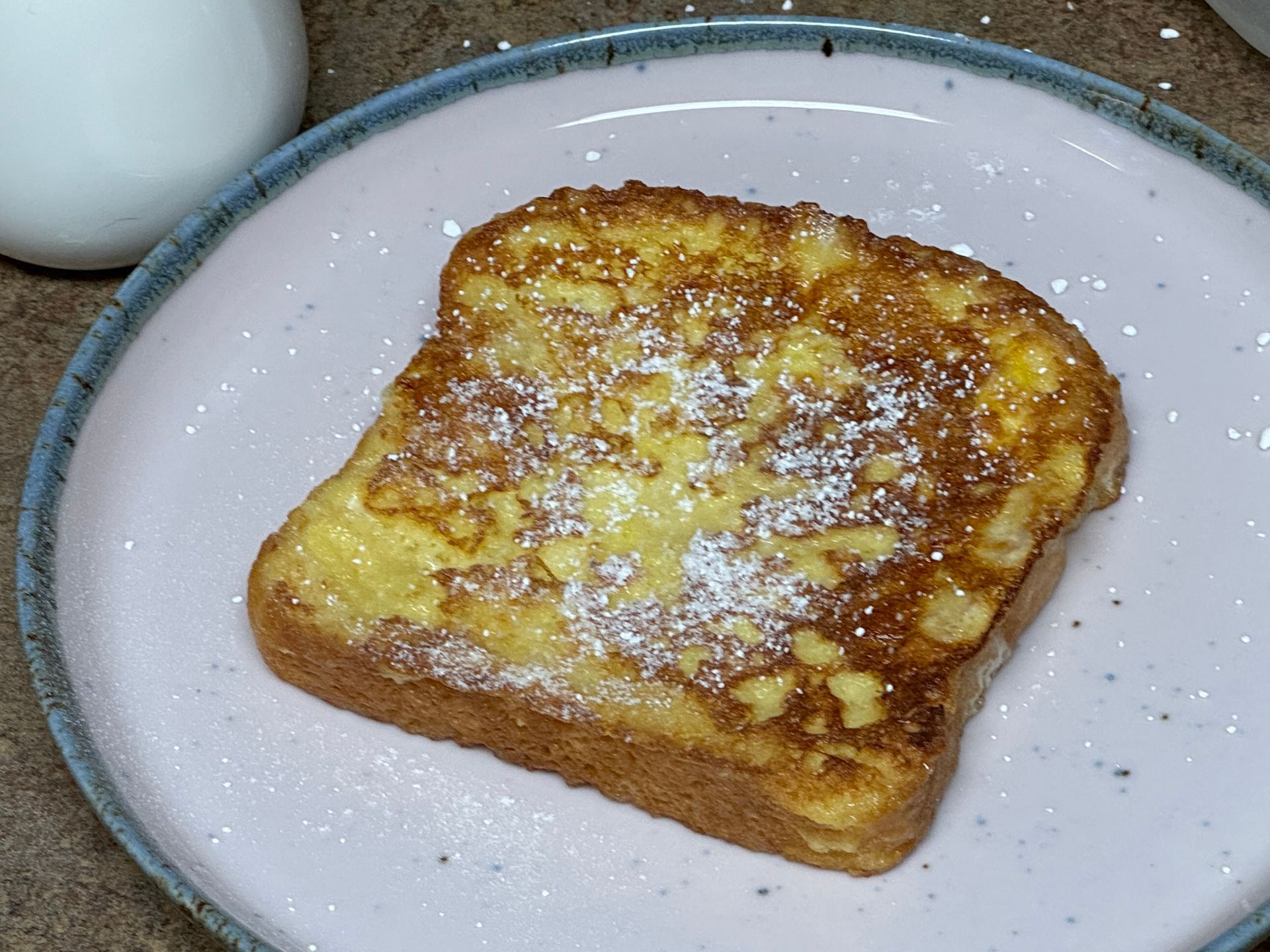 A slice of french toast with powdered sugar on a pink plate