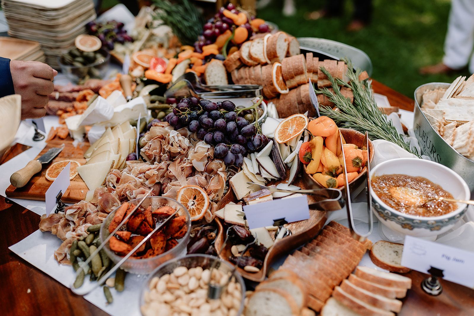 Charcuterie spread with cheeses, grapes, bread, nuts, and dips on a table outdoors