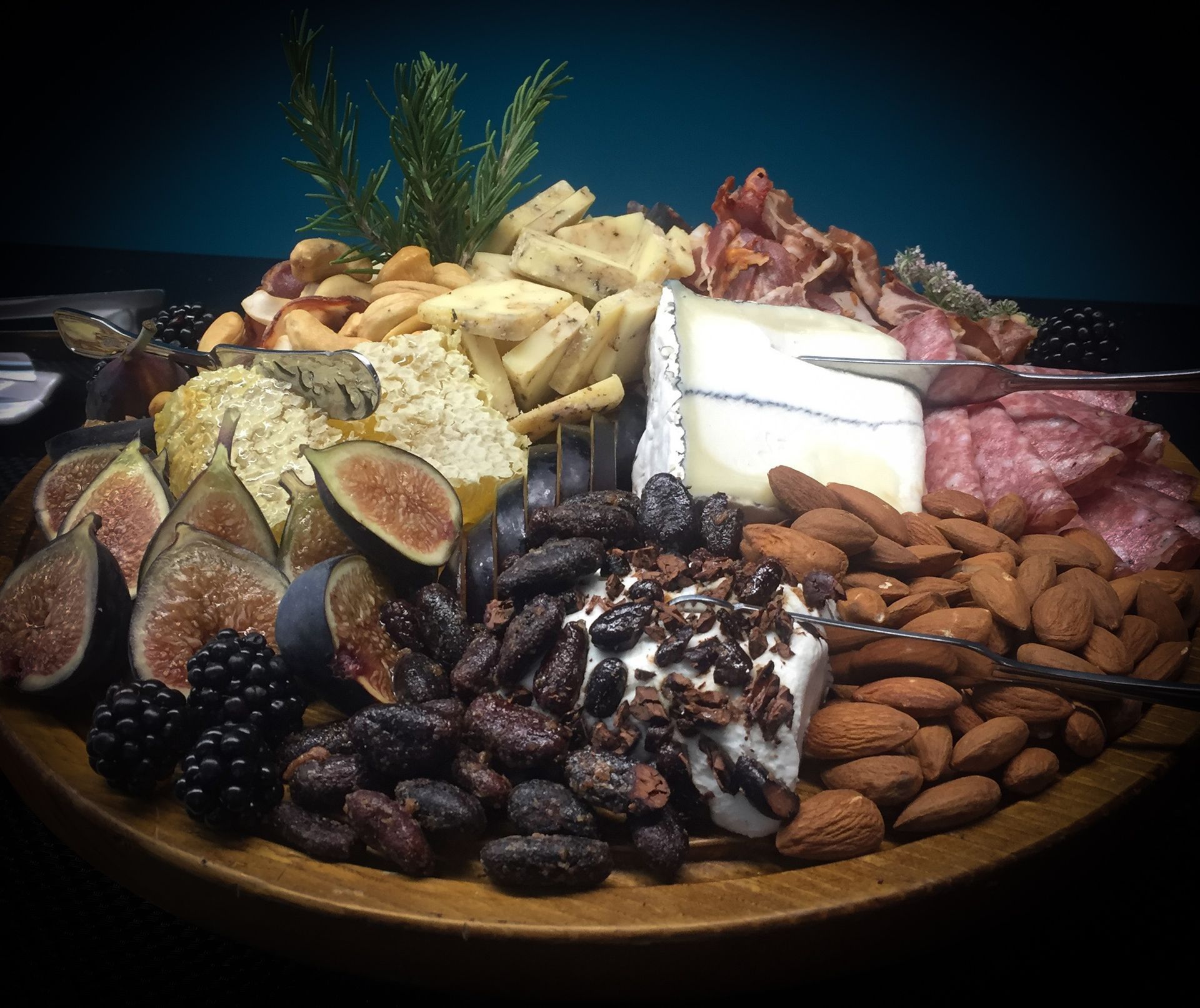 Assorted cheeses, cured meats, nuts, and dried fruits arranged on a wooden platter.