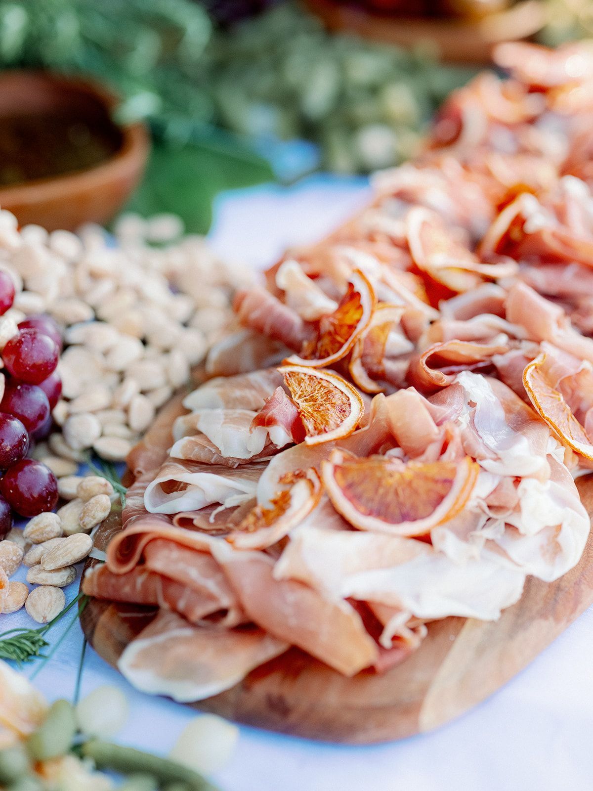 Assorted sliced cured meats and crackers on a wooden platter at a buffet table