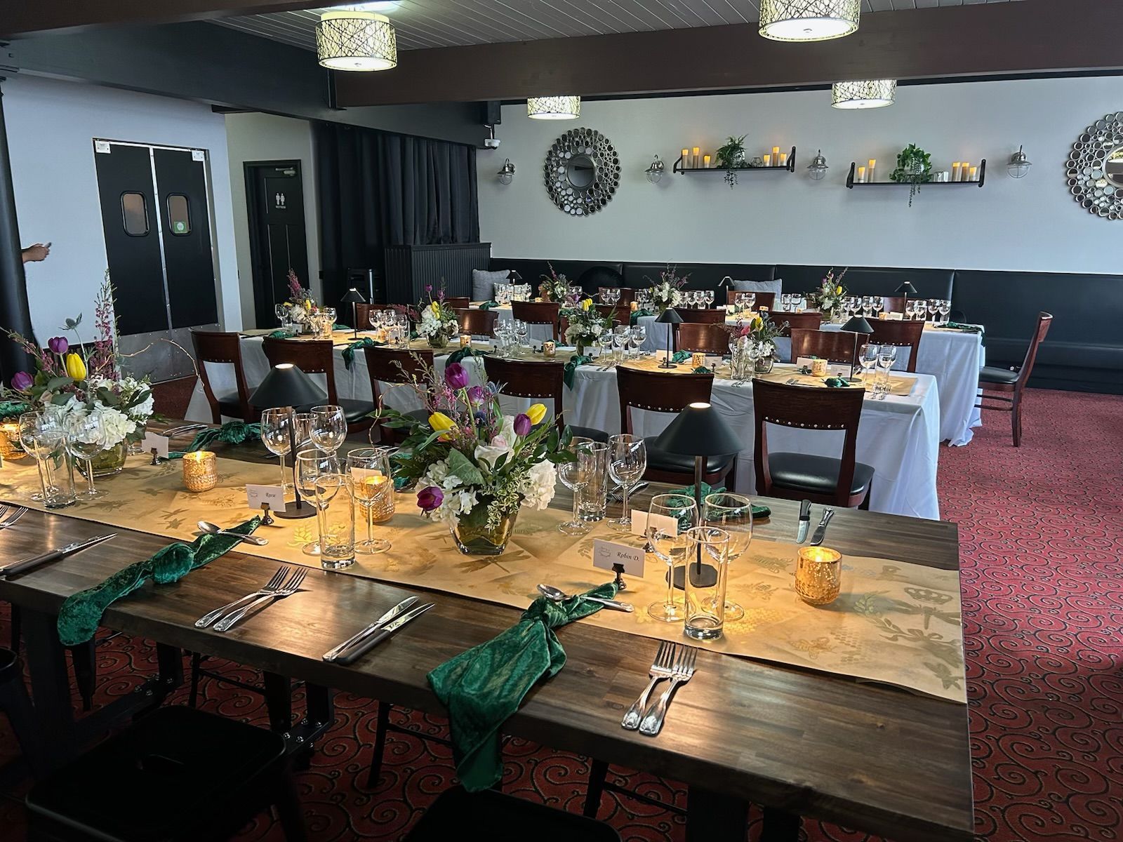 Decorated banquet hall with set tables, floral centerpieces, green napkins, and pink carpeting