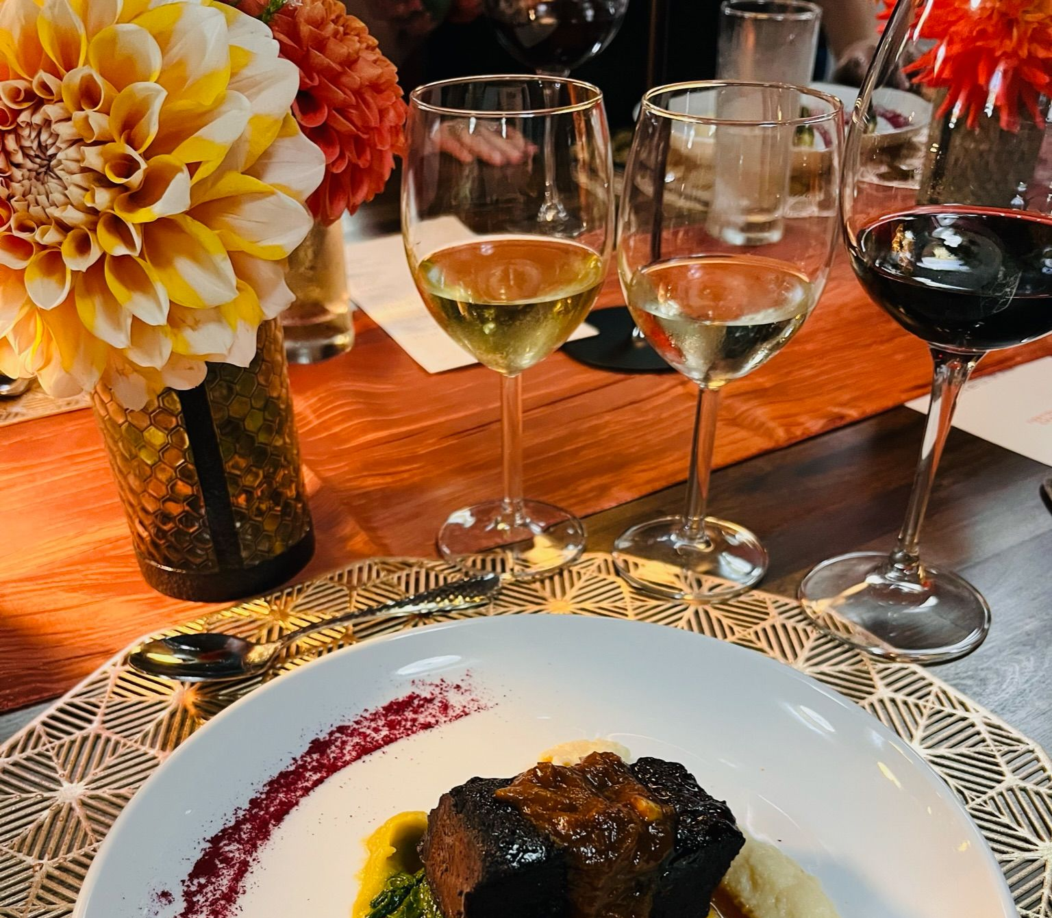 Plate with food, wine glasses, and flowers on a table.