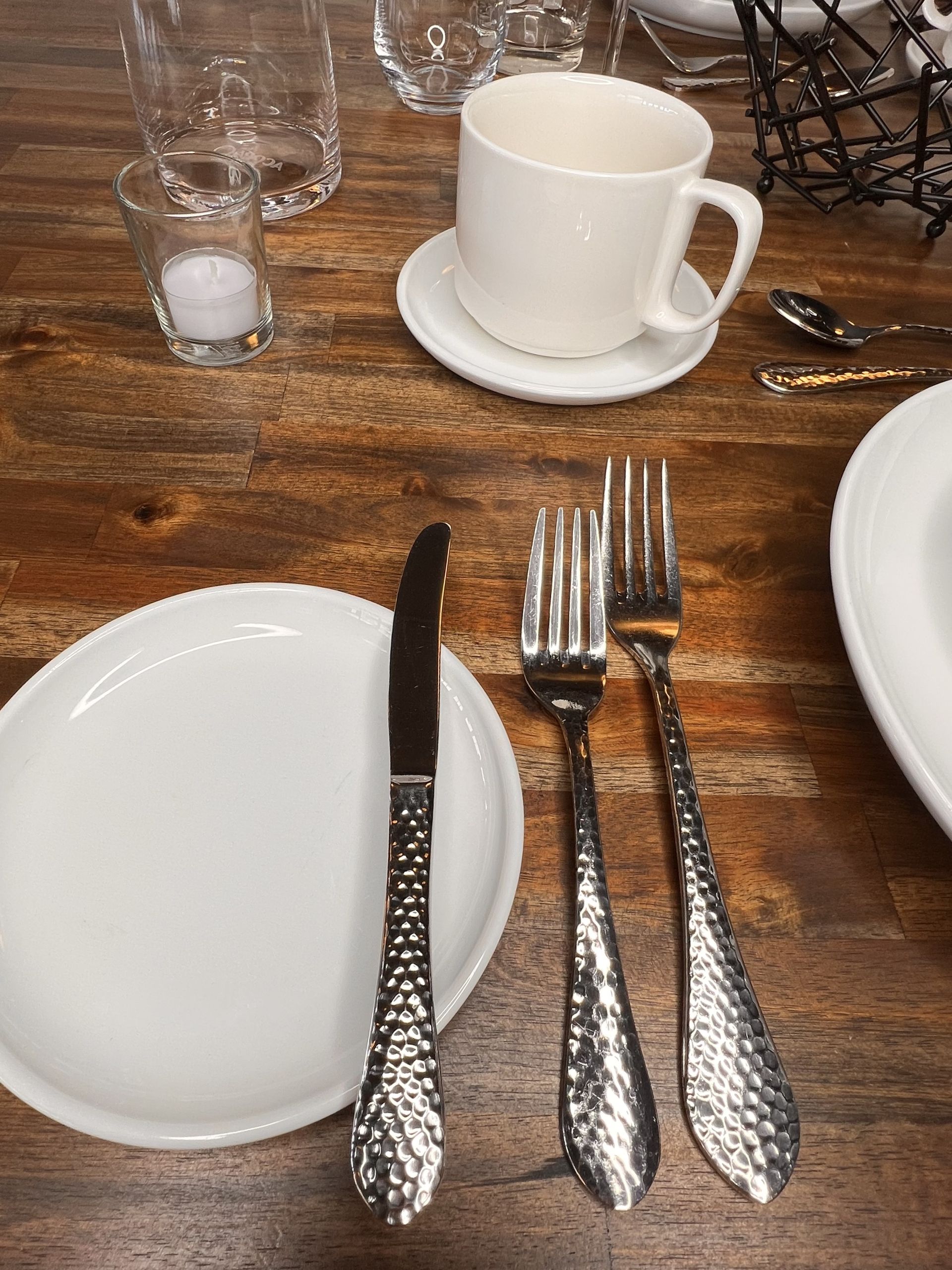 Table setting with white plates, ornate silverware, a white coffee cup, and a salt shaker on a wooden table