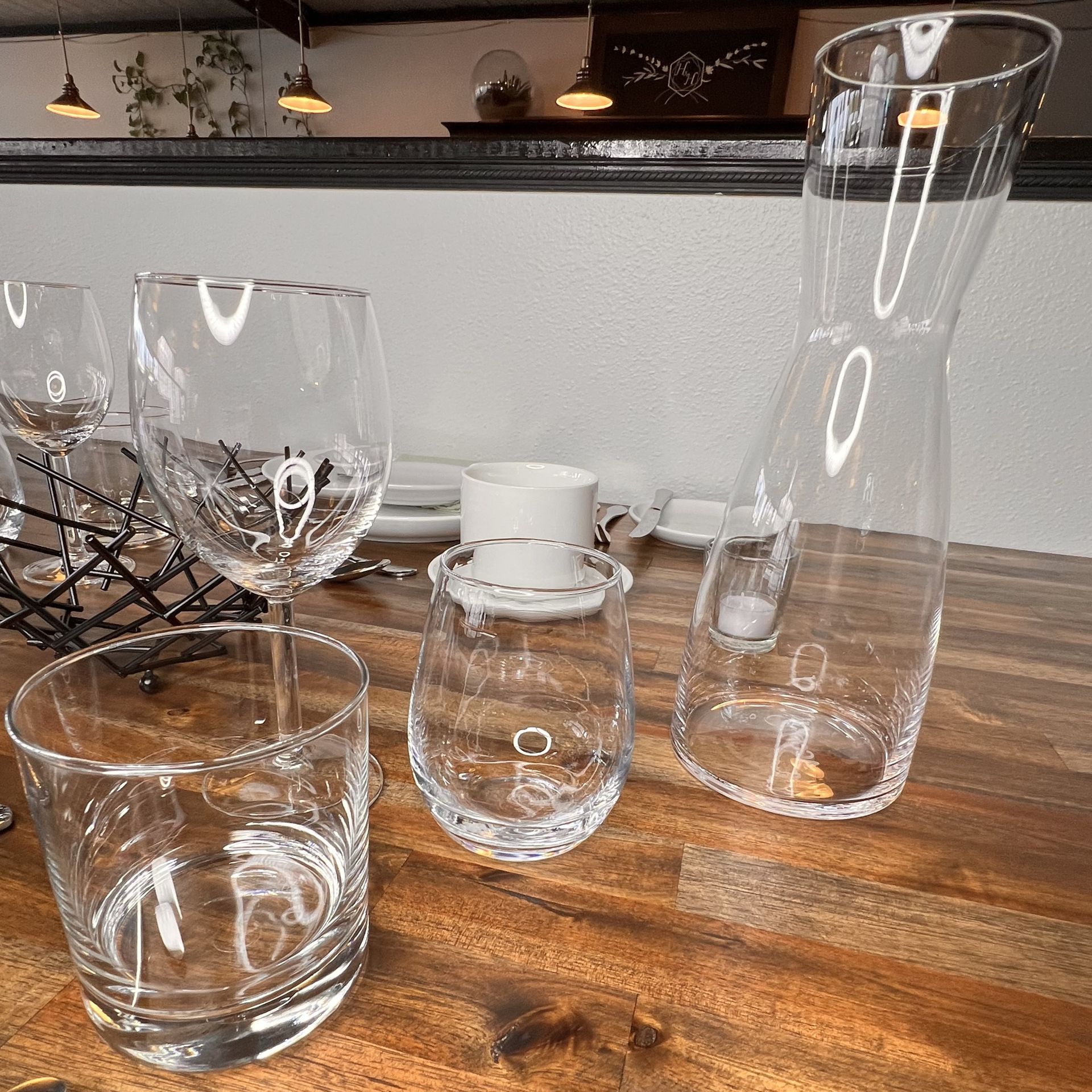 Assorted clear glassware and a white cup arranged on a wooden table in a showroom