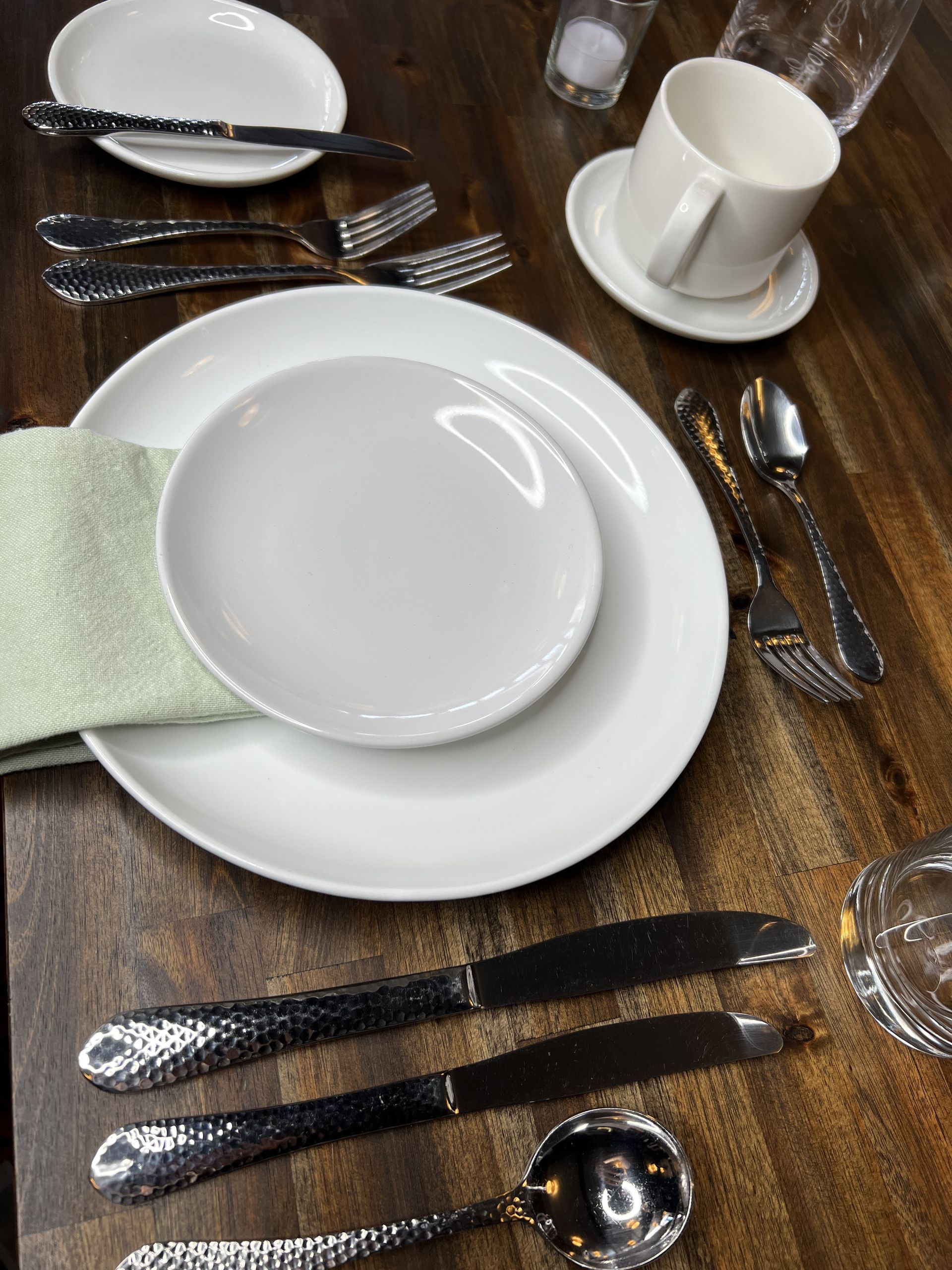 Table setting with white plates, cups, and silverware on a wooden surface.