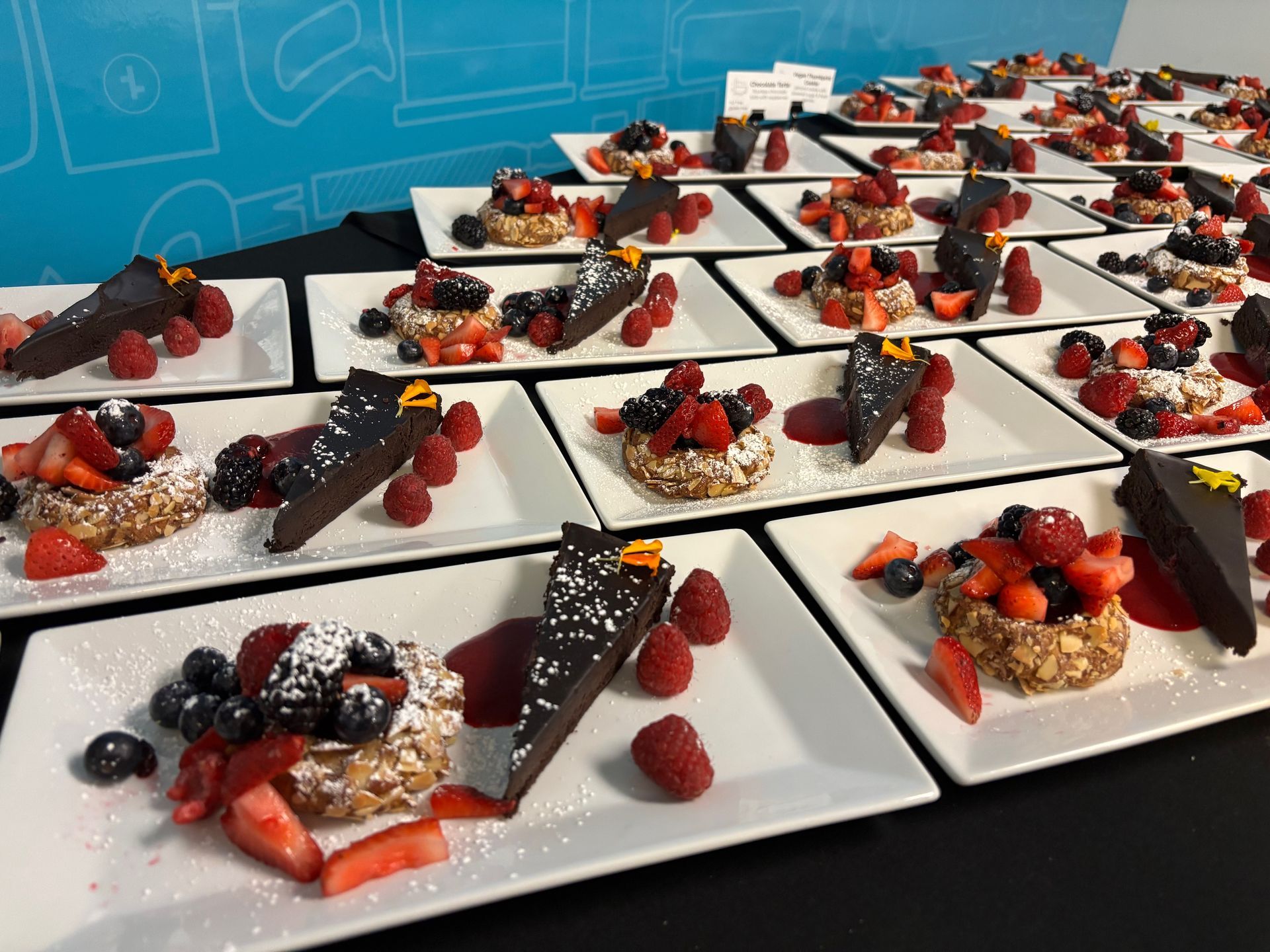 Desserts plated on white squares, with berries, nuts, and chocolate cake.