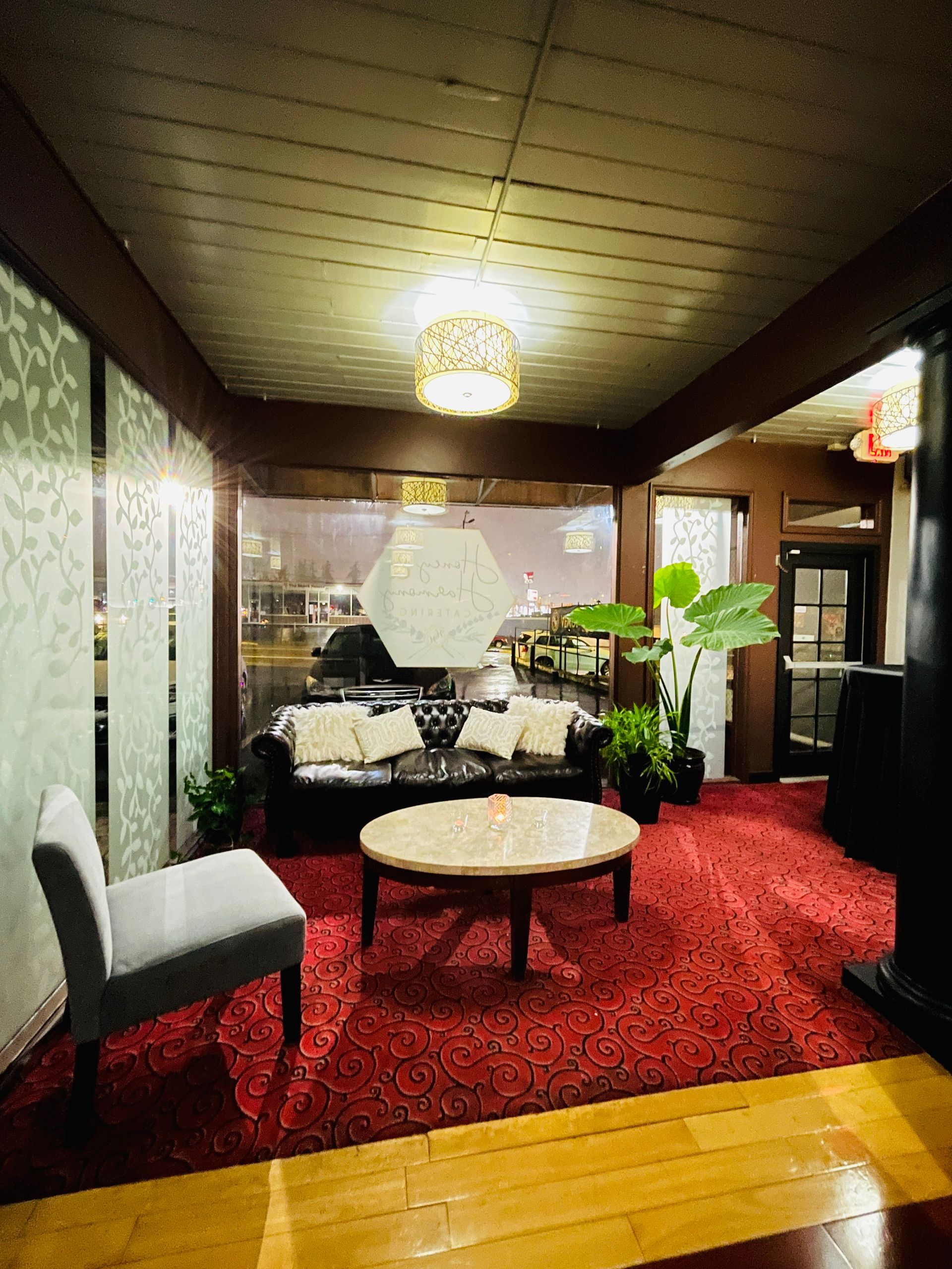 Cozy lounge with red carpet, white chairs, round table, plants, and warm ceiling light