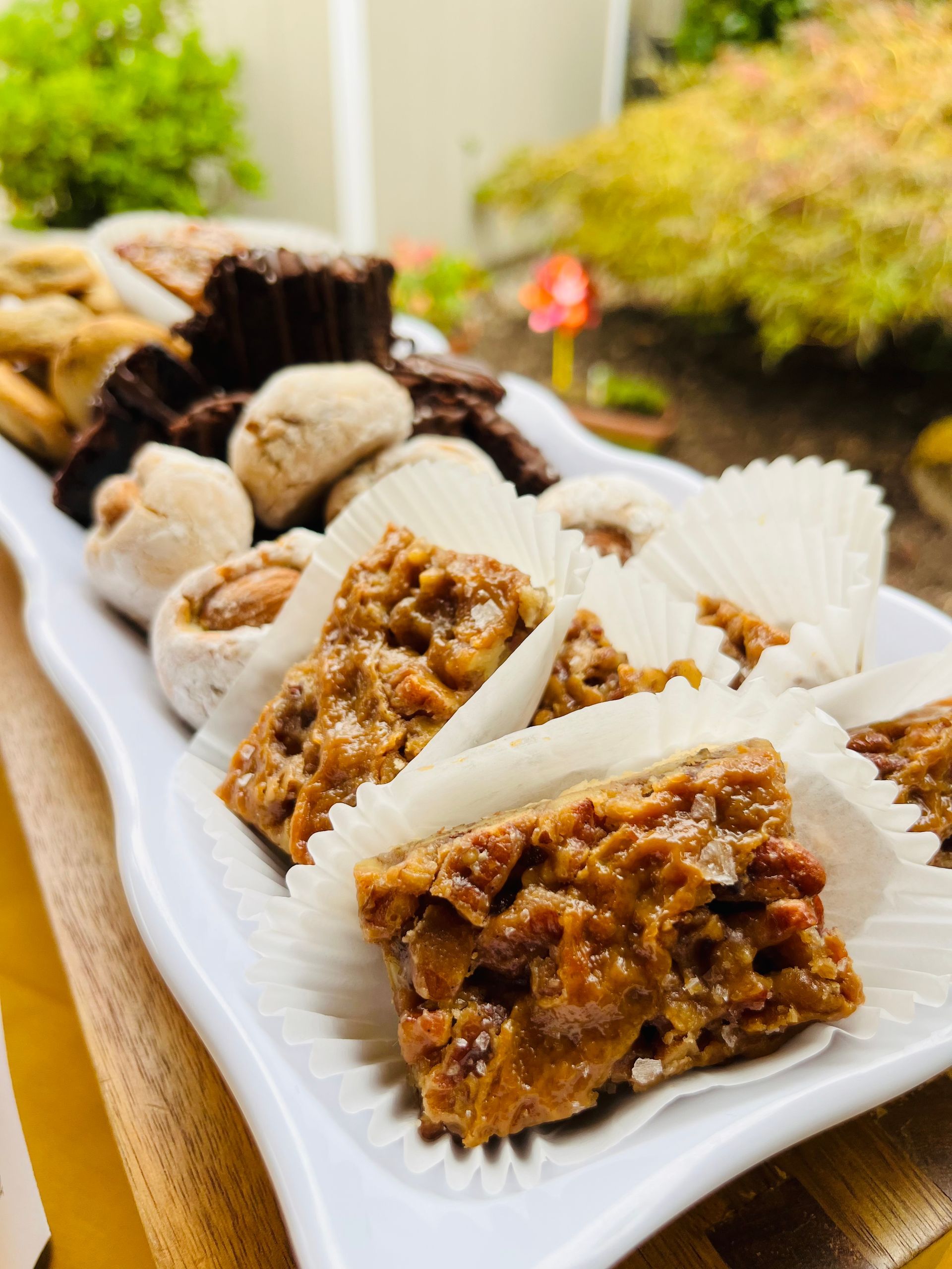 White platter of assorted cookies outdoors, with a blurred green background.