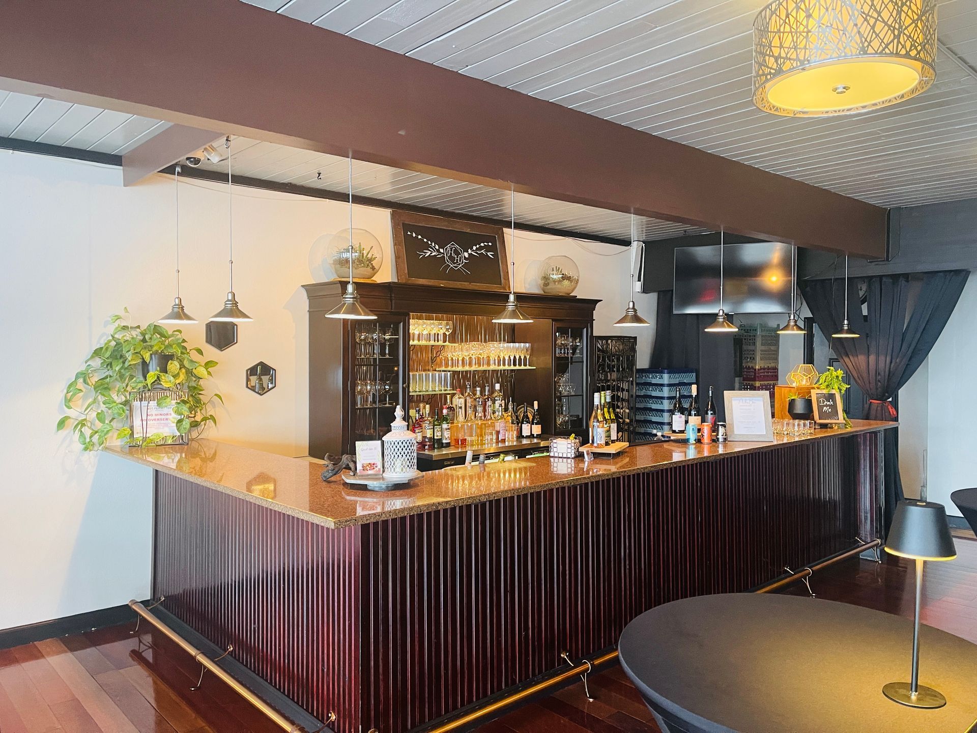 Stylish hotel bar with dark wood counter, shelves of bottles, hanging lights, and a round table in front