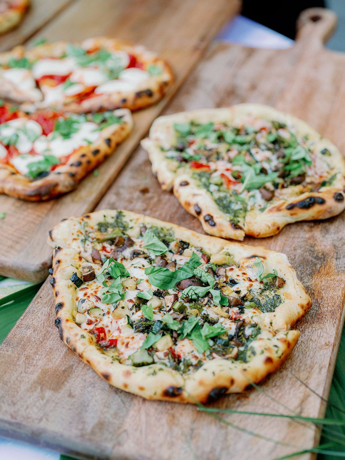 Several flatbread pizzas topped with herbs, cheese, and vegetables arranged on rustic wooden serving boards.