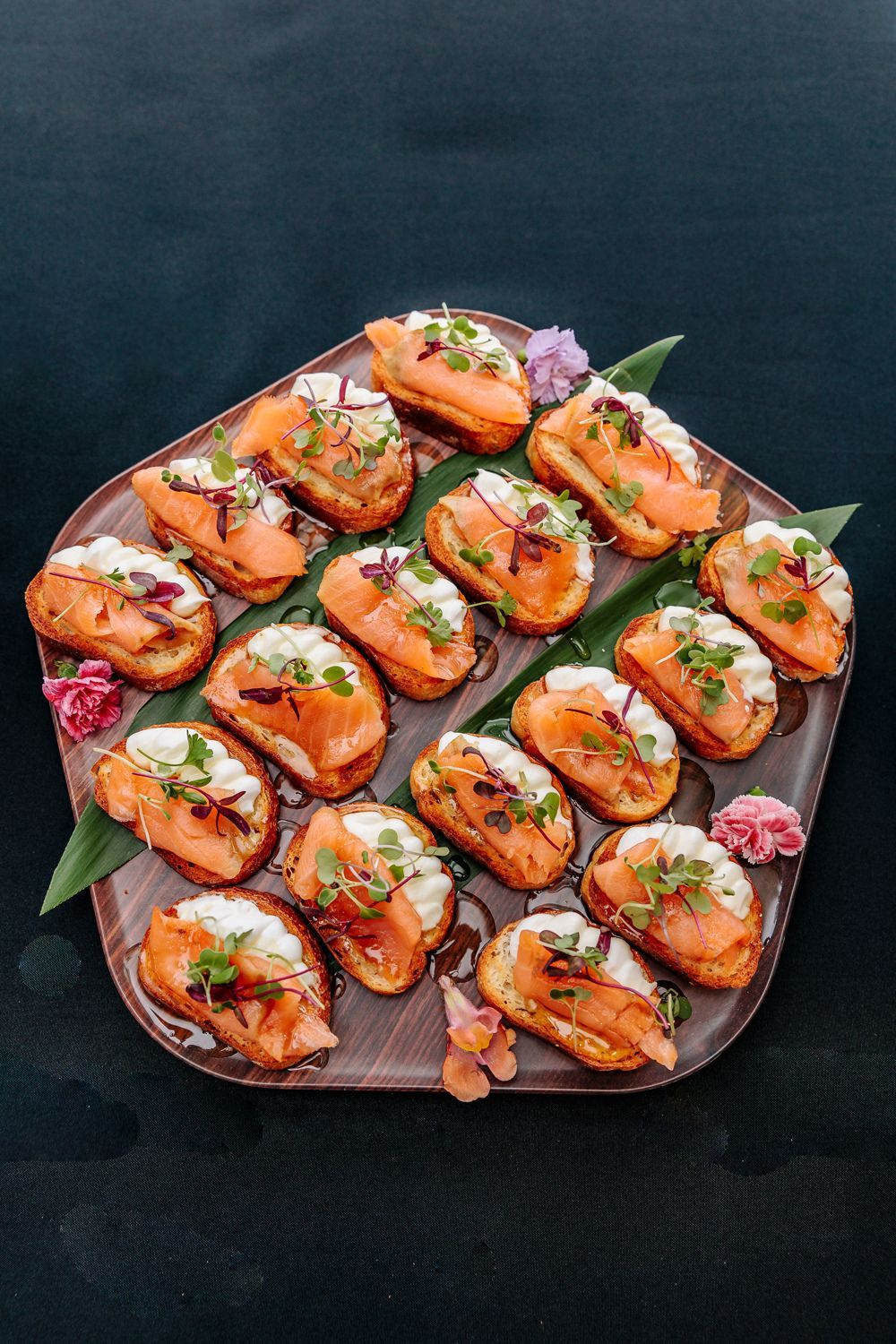 A platter of smoked salmon crostini topped with cream cheese and fresh herbs, garnished with edible flowers.