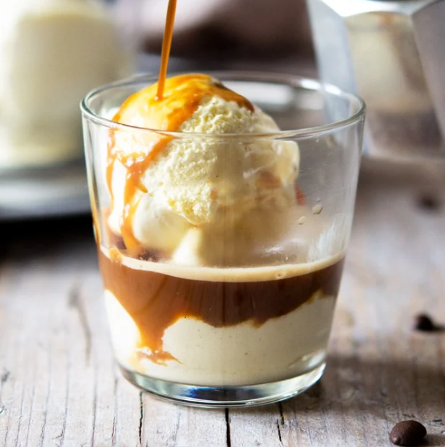 Affogato in a glass: vanilla ice cream with espresso being poured over, on a wooden surface.