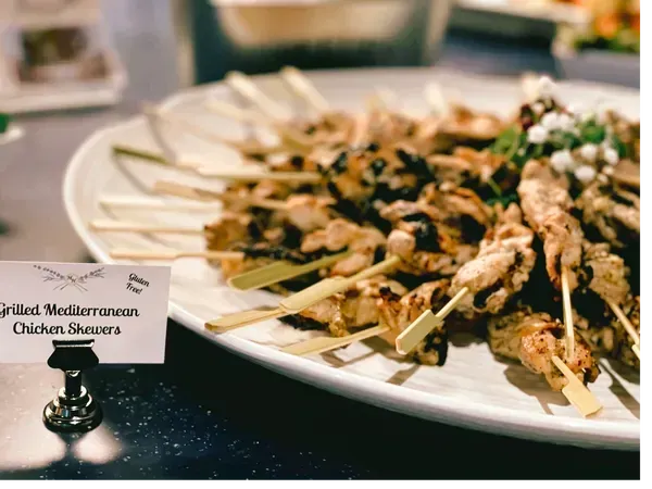 A platter of grilled Mediterranean chicken skewers with a small sign labeling the dish next to it.
