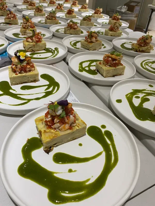 Many plates, each featuring a square serving of food topped with a mixture and a decorative swirl of green sauce.