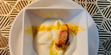 A single lobster claw served in a white square bowl with white cream and a dusting of yellow garnish.