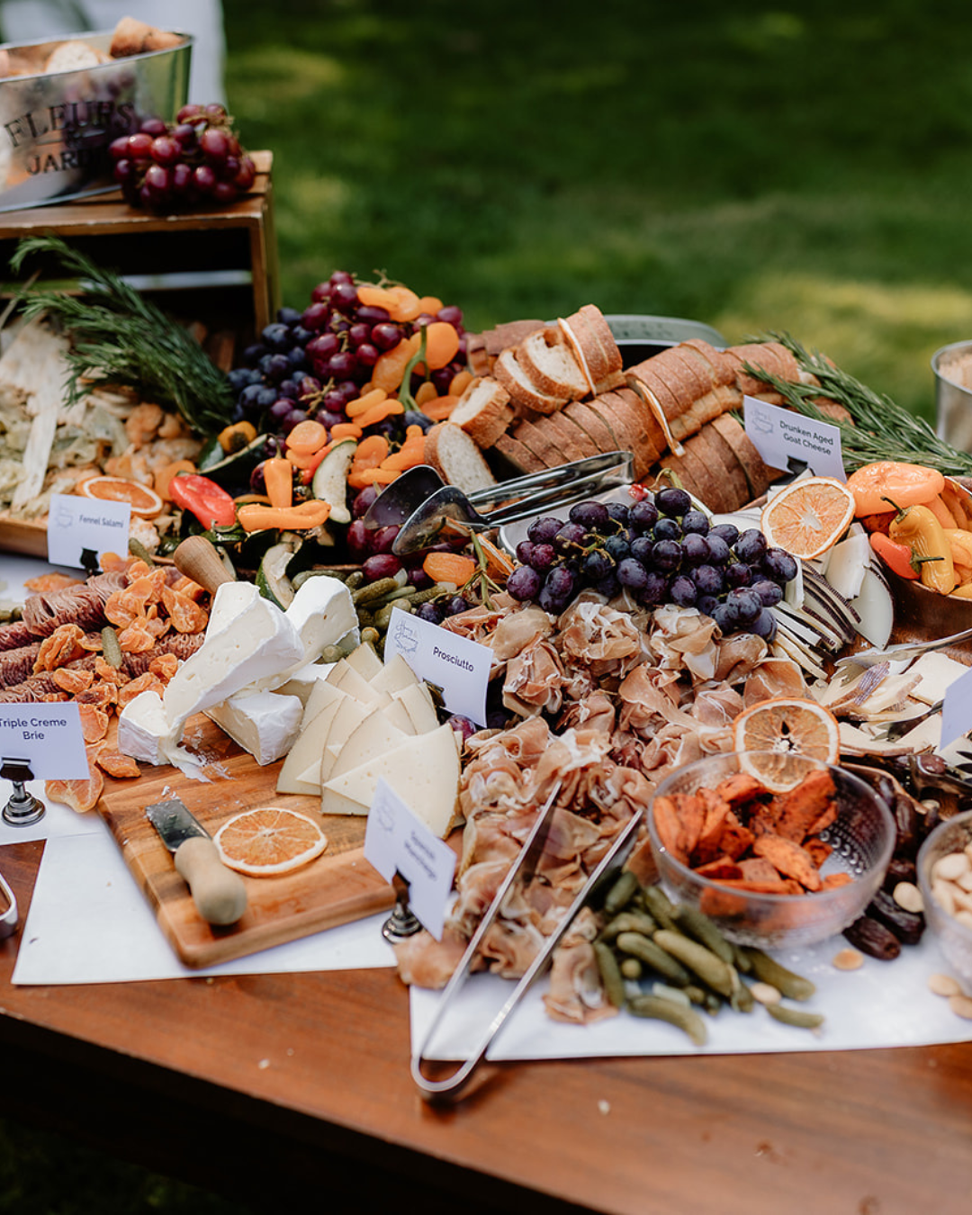A beautifully arranged charcuterie spread with cheeses, meats, fresh and dried fruits, bread, and pickles on a table.