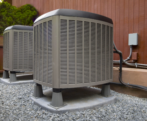 Two air conditioners are sitting on top of gravel outside of a building.