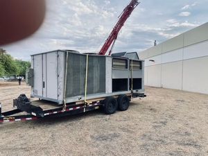 A trailer with a large unit on it is being lifted by a crane.