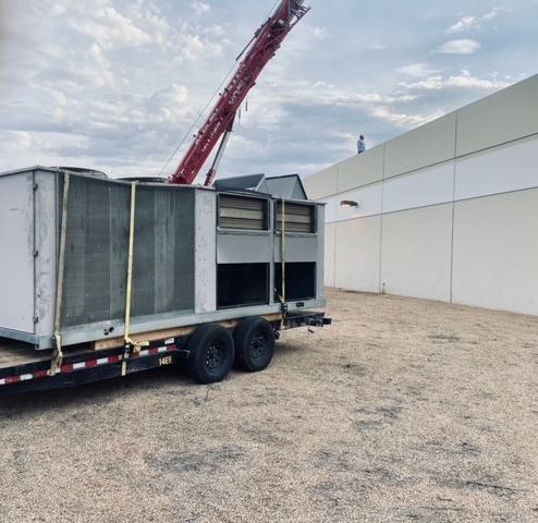 A trailer with a crane attached to it is parked in front of a building