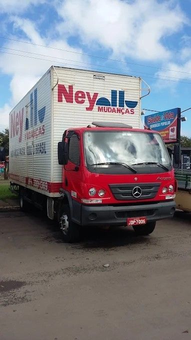 Um caminhão de entregas da Ney Mudanças vermelho estacionado em uma rua sob um céu azul parcialmente nublado.