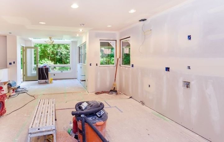 Renovated living room with white walls, recessed lights, plastic-covered floors, and an open doorway to greenery.