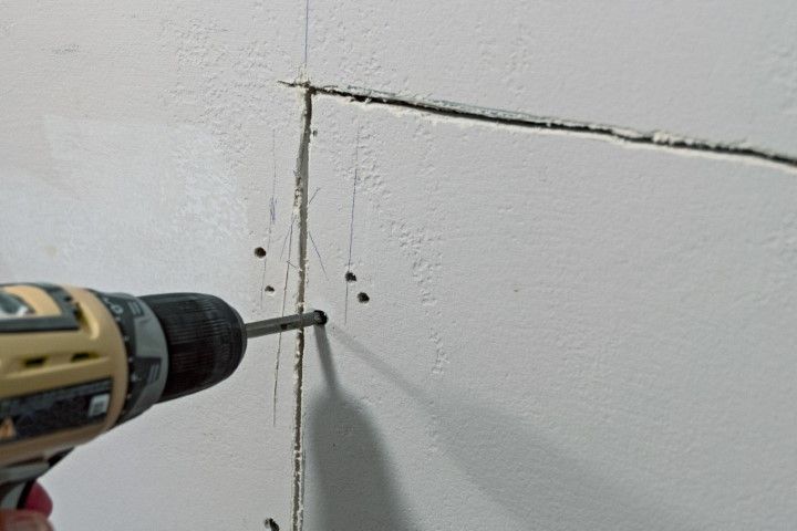 Cordless drill drilling a hole in a white wall corner seam