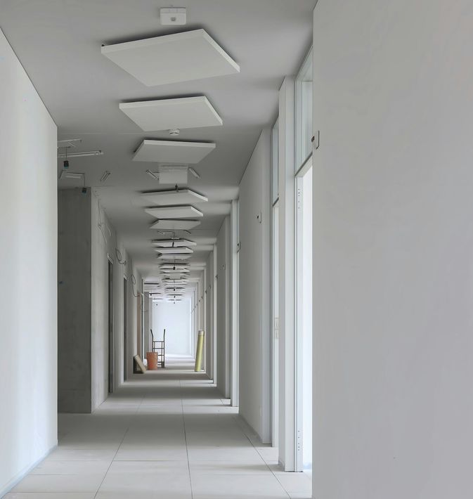Empty white hallway with repeating ceiling lights and doors, viewed in perspective toward the far end