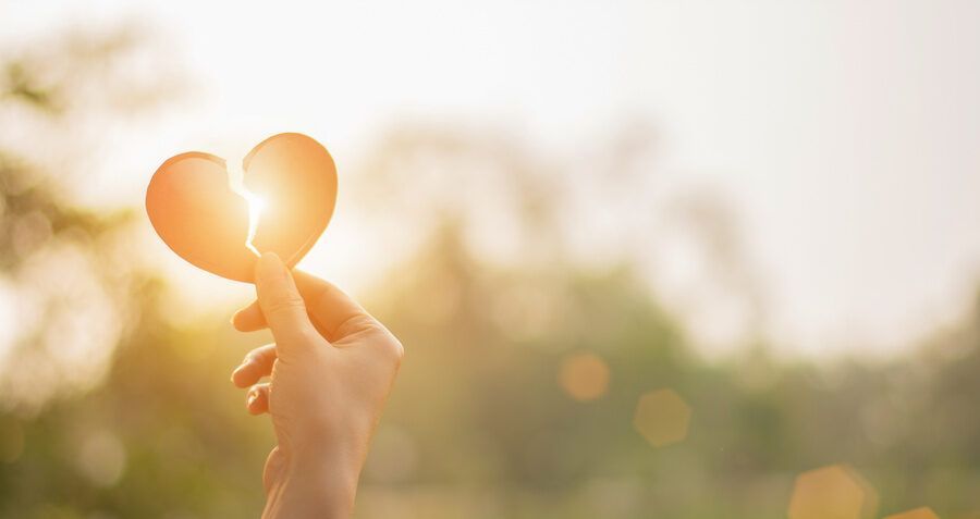 Hand holding a heart-shaped cutout in warm sunlight, with a blurred outdoor background