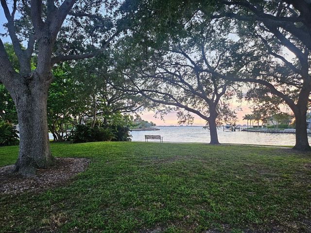 Park with large trees and grassy lawn overlooking a calm waterfront at sunset