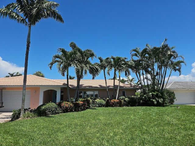 Single-story house with a red tile roof, palm trees, and a green lawn under a bright blue sky