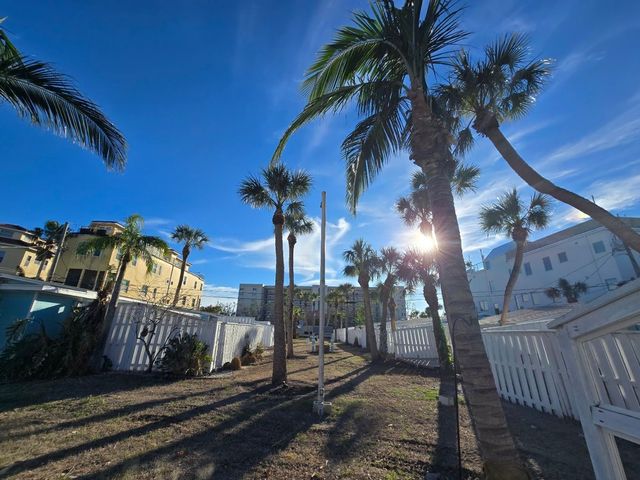 Sunny palm-lined courtyard with white buildings and blue sky, sunlight shining through tall trees