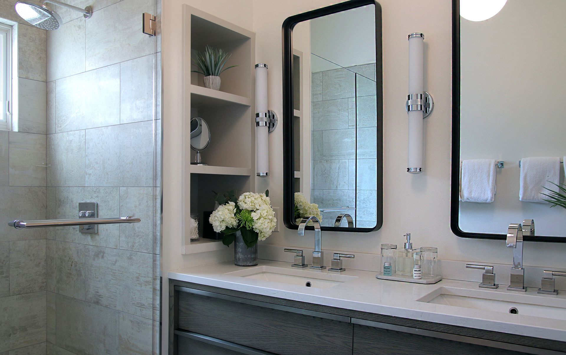 A bathroom with two sinks , two mirrors and a walk in shower.