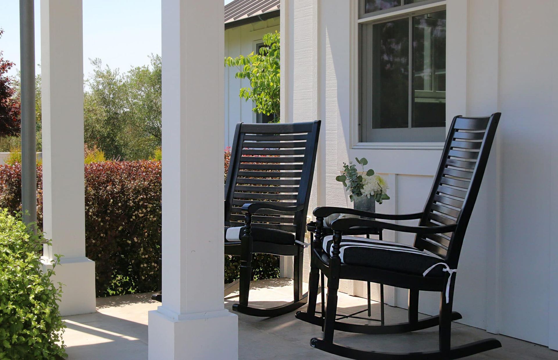 Two rocking chairs are sitting on a porch next to a window.