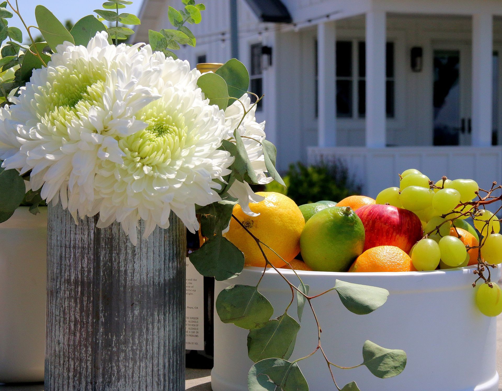 A vase of flowers sits next to a bowl of fruit